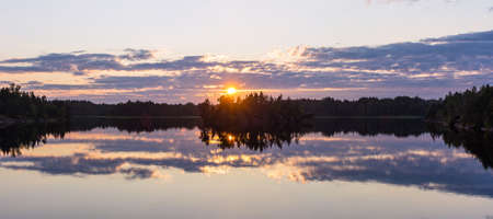 Panorama of a beautiful summer sunset on a forest lakeの写真素材