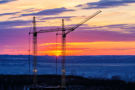 Construction cranes against a bright sunset background