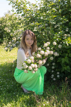 Slender girl in a summer park near a flowering bush