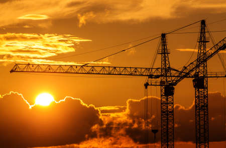 Silhouettes of building cranes against sunset backgroundの写真素材