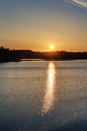 the last rays of the sun at sunset over a forest lakeの写真素材