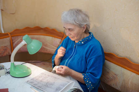 elderly woman at the table is engaged in embroideryの写真素材