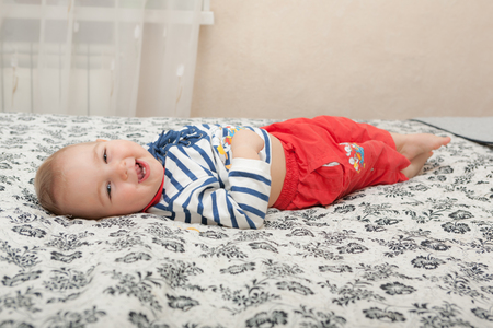 cheerful baby lying on the bed at homeの写真素材