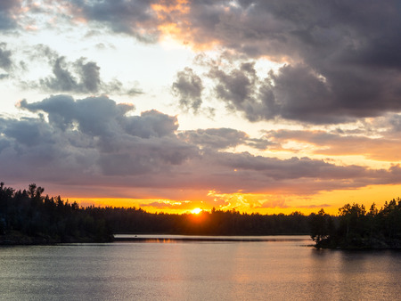 bright sunset with clouds over a forest lakeの写真素材