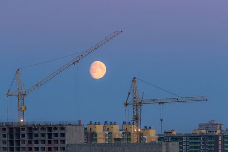 construction cranes under the moon in the morningの写真素材