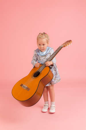 little girl with a guitar on a pink backgroundの写真素材