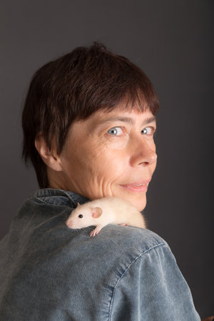 studio portrait of woman with white baby rat on black backgroundの写真素材
