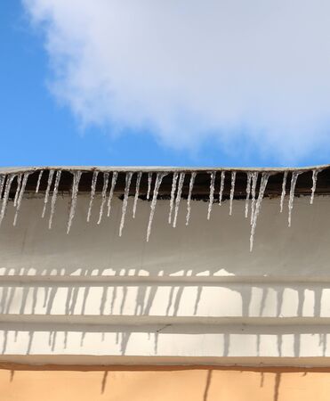 roof of the house with icicles and the wall, the spring sky and sunの写真素材