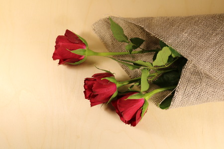 A bouquet of dark red roses wrapped in a mat on a wooden backgroundの写真素材