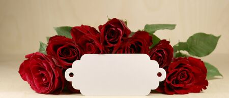 A bouquet of dark red roses with a white blank label on a wooden backgroundの写真素材