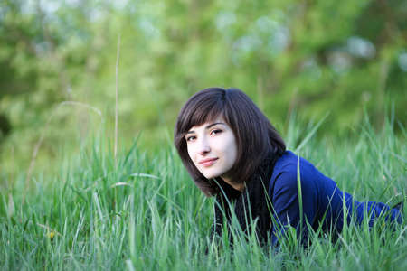 Portrait of young beautiful woman lying in green summer fieldの写真素材