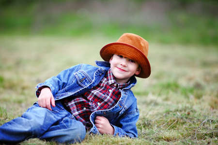 Happy smiling boy dressed in country style playing in the park near sunset with shallow depth of field and copy space to left and right の写真素材
