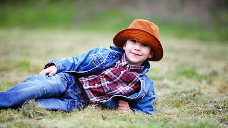 Happy smiling boy dressed in country style playing in the park near sunset with shallow depth of field and copy space to left and right の写真素材