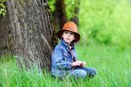 Happy smiling boy dressed in country style playing in the park near sunset with shallow depth of field and copy space to left and right の写真素材