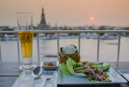 A glass of beer in front of chaopraya river with sunsetの写真素材