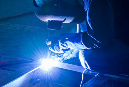 Welder working a welding metal work with protective mask and sparks for constructionの写真素材