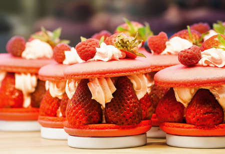 Strawberry and raspberry macarons on a white table with fresh fruitsの写真素材