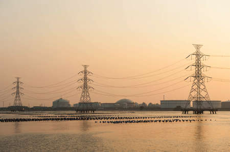 high voltage post.High-voltage tower over oil and gas tanker background.の写真素材