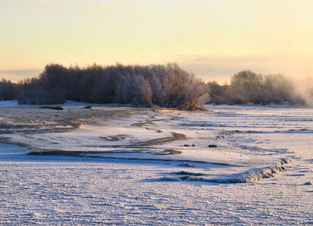 Trees on the sandy bank of the Ob River are covered with early snow. Mist over the first ice. Yellow sky dawn. Landscape in golden-blue tonality. Nature of Siberia, Novosibirsk region, 2018の写真素材
