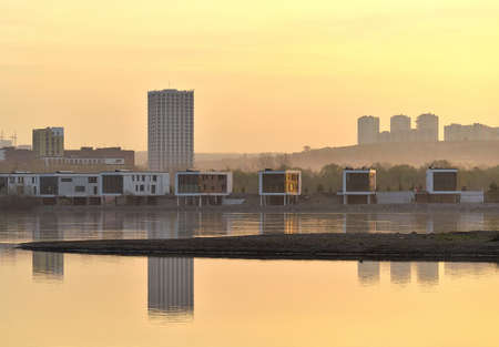Modern houses on the banks of the great Siberian river in the city of Novosibirsk in the early morning. Reflections in the water, Golden sky. Russia, Novosibirsk, 2020の写真素材