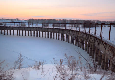 Dam on the pond on a winter morning. The arc of a concrete dam on a frozen winter pond near Novosibirsk. Morning Golden sky. Rural architectural "classicism". Siberia, Russia, 2018の写真素材