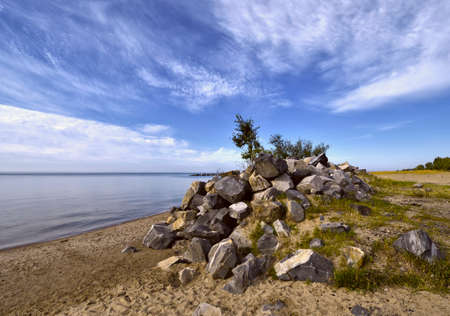 Stone hill on the Bank of the river. A pile of stones on the sandy shore of the Novosibirsk reservoir near Novosibirsk. White feathery clouds in the clear sky. Siberia, Russia, 2019の写真素材