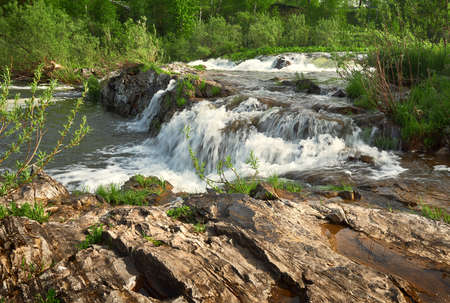 Rapids on the Suenga river. Stone Bank of a mountain river, streams of water with white foam, green vegetation on the Bank in spring. Pure nature of Siberia, a landscape without people. Novosibirsk region, Russia, 2020の写真素材