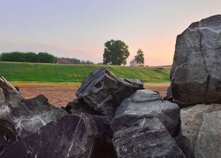 Big stones in the morning sun, a lonely house with trees on a green slope in the distance, the morning clear blue sky, nature of Siberia. Novosibirsk region, Russia, 2020の写真素材