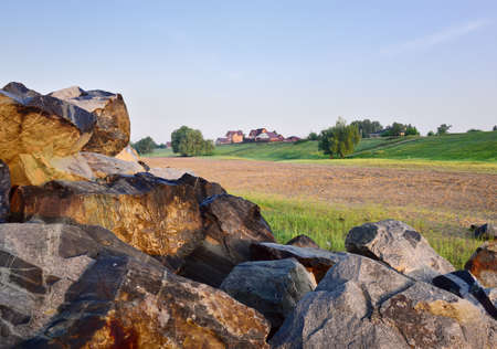 Big stones in the morning sun, a lonely house with trees on a green slope in the distance, the morning clear blue sky, nature of Siberia. Novosibirsk region, Russia, 2020の写真素材