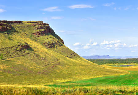 Rocky cliffs in the steppe in summer under a blue cloudy sky. Siberia, Russia
