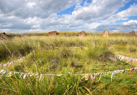The burial mound of the 5th century BC, steles of red stone with ritual ribbons under a cloudy sky....