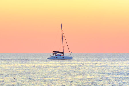A sailing boat on the horizon against the pink background of the evening sky. Sochi, Russia, 2021