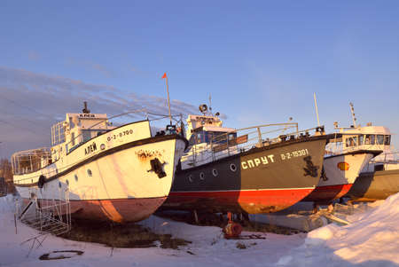 Novosibirsk, Siberia, Russia-04.03.2021: Boats and yachts in winter. River boats wintering on the shore among the snowdrifts in the lock area against the background of the evening skyのeditorial素材