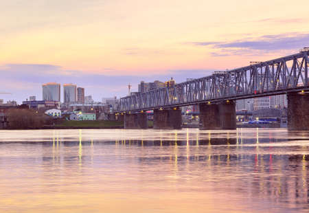 Novosibirsk, Siberia, Russia-05.03.2021: Morning on the Ob River. Steel bridge of the Trans-Siberian Railway, high-rise buildings on the shore against the backdrop of a picturesque golden dawn skyのeditorial素材
