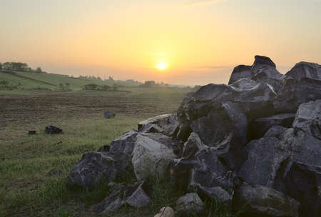 A pile of large stones, a sandy beach and a coastal slope in the distance, the rising sun on the horizon, the Golden clear sky, nature of Siberia. Novosibirsk region, Russia, 2020の写真素材