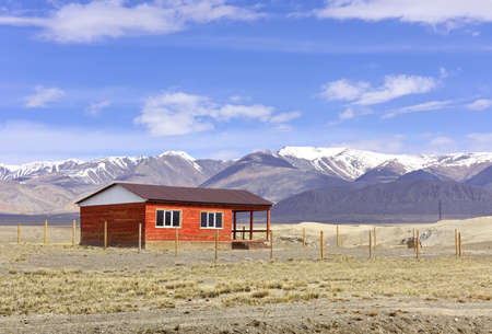 A house in the Altai Mountains. A lonely building in the Chui steppe in spring against the background of the snow-covered Kurai ridge under the blue sky. Siberia, Russiaの写真素材