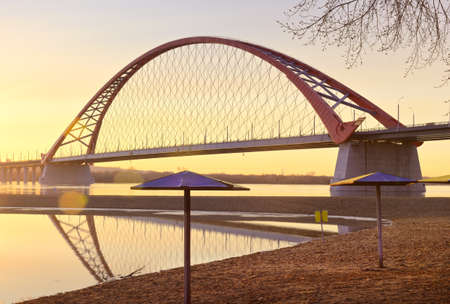 Dawn of the Bugrinsky Bridge. A deserted beach in spring, an arched modern road bridge over the Ob River in golden light. Novosibirsk, Siberia, Russiaの写真素材