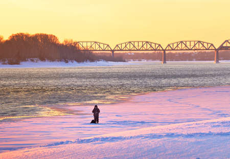 Novosibirsk, Siberia, Russia-02.07.2021: Fisherman on the ice of the Ob River, railway bridge in the distance in the bright morning lightのeditorial素材