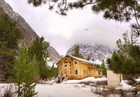 Gorny Altai, Siberia, Russia, 05.05.2021: Aktru Valley in the Altai Mountains. The wooden house of the tourist base is surrounded by pine trees and mountains, drowning in cloudsのeditorial素材