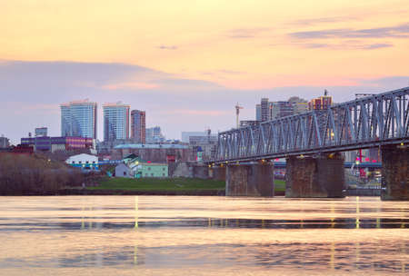 Novosibirsk, Siberia, Russia-05.03.2021: Morning on the Ob River. Steel bridge of the Trans-Siberian Railway, high-rise buildings on the shore against the backdrop of a picturesque golden dawn skyのeditorial素材