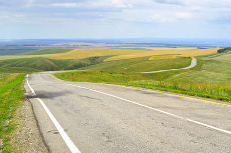 A regional road in a rural area in the steppe against the background of green hills under a cloudy...