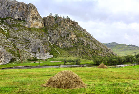A haystack on a pasture against a high cliff under a blue cloudy sky. Siberia, Russia
