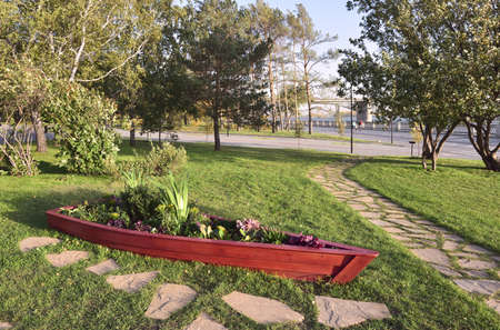 Novosibirsk, Siberia, Russia - 09.10.2019: Decorative boat with flowers in the Park embankment of the Ob river in Novosibirsk. Stone path, trees, green lawn, bridge on the horizonの写真素材