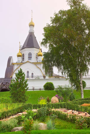 Alpine garden at the foot of the tent Orthodox church behind the monastery fence on a foggy morning. Krasnoyarsk, Siberia, Russiaの写真素材