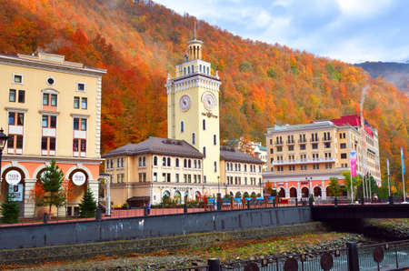 Rosa Khutor, Sochi, Russia, 11.01.2021. The village "Rosa Khutor". Town Hall with clock on the embankment of the Mzymta River among the autumn mountains of the Caucasusのeditorial素材