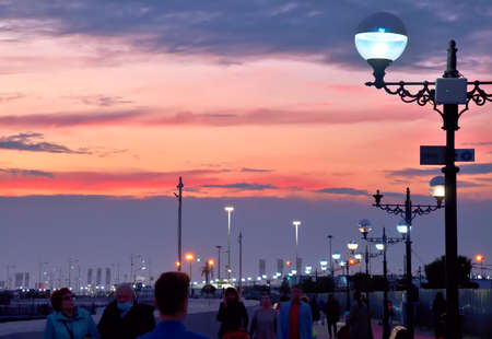Adler, Sochi, Russia, 11.01.2021. Evening embankment of the Black Sea. People walk under street lights against the sunset skyのeditorial素材