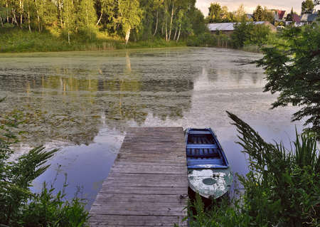 forest pond in summer. A boat at a wooden pier on the water with the reflection of trees....