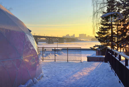 Winter embankment in the evening. A platform covered with snow on the background of a Communal bridge over the Ob River in a big city. Novosibirsk, Siberia, Russia, 2022の写真素材