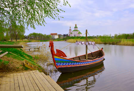Tourist boat at the pier. Drakkar on the river, Elijah Church on the horizon, architecture of the XVIII century. Suzdal, Russia, 2022の写真素材