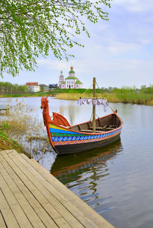 Tourist boat at the pier. Drakkar on the river, Elijah Church on the horizon, architecture of the XVIII century. Suzdal, Russia, 2022の写真素材